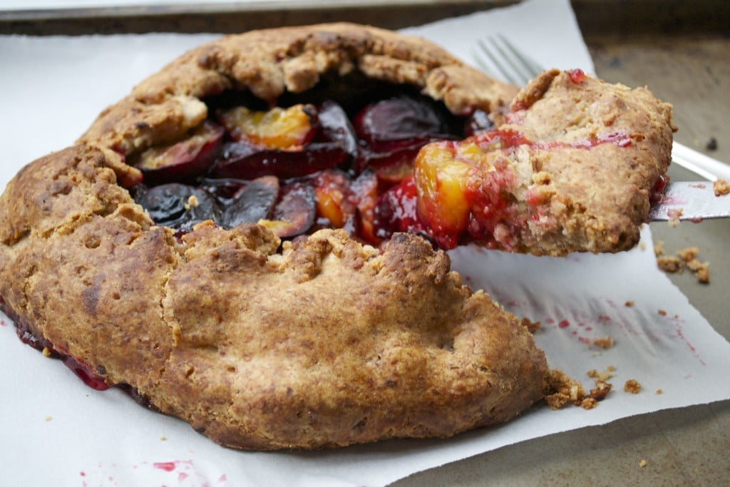 A plum galette on a baking sheet with a slice being removed.