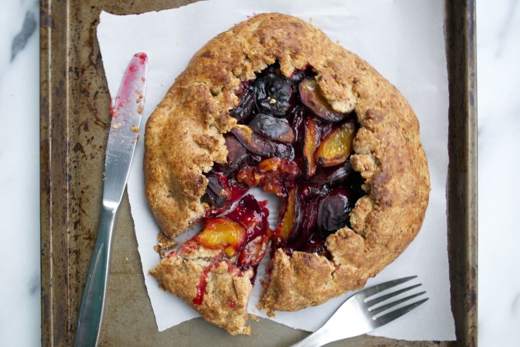 A plum galette on a baking sheet with a fork and knife.
