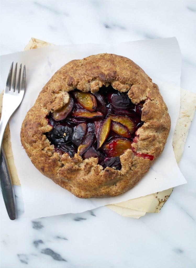 A plum galette on a piece of parchment paper with a fork. 
