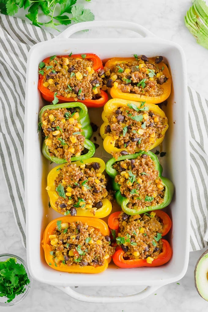 A large baking dish filled with colorful stuffed bell peppers with quinoa, beef, corn, and fresh cilantro. 