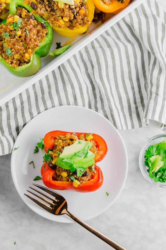 A small plate with a beef stuffed bell pepper topped with avocado and a fork.