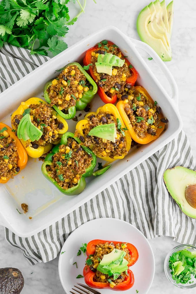 A baking dish with stuffed peppers filled with quinoa and beef and topped with avocado.