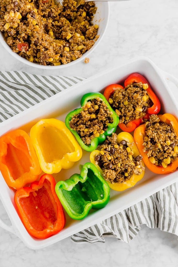 A baking dish filled with bell peppers of different colors being stuffed with a beef and quinoa mixture. 