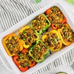 A baking casserole dish filled with colorful stuffed bell peppers with quinoa, beef, corn, and fresh cilantro.