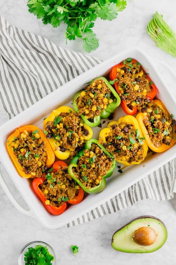 A baking casserole dish filled with colorful stuffed bell peppers with quinoa, beef, corn, and fresh cilantro.