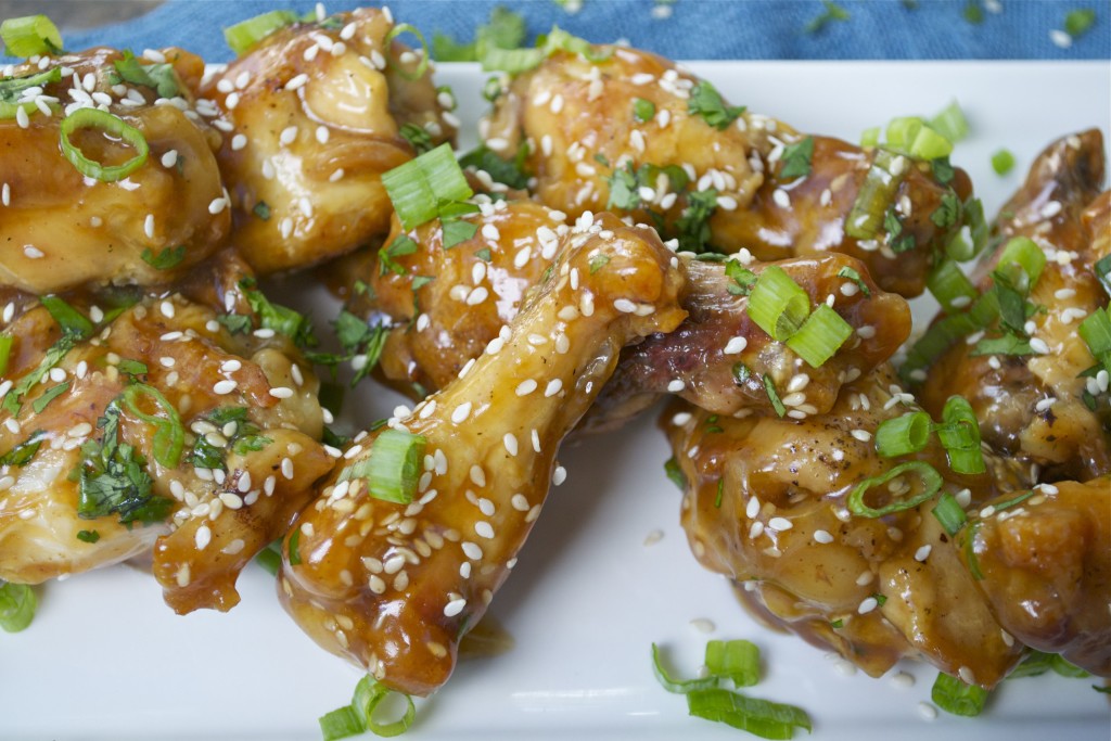 A pile of teriyaki chicken wings topped with green onions and sesame seeds on a white platter.