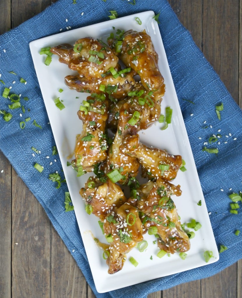 A platter of teriyaki chicken wings topped with green onions and sesame seeds.