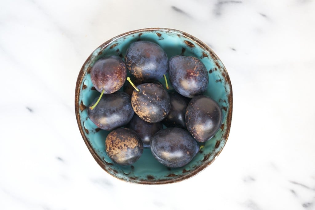A bowl of Italian plums on a marble table.