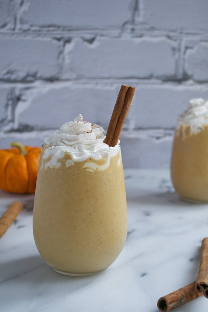 A glass of pumpkin spice latte milkshake topped with whipped cream and a cinnamon stick.