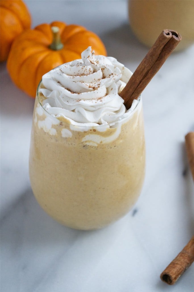 A glass of pumpkin spice latte milkshake topped with whipped cream and a cinnamon stick.