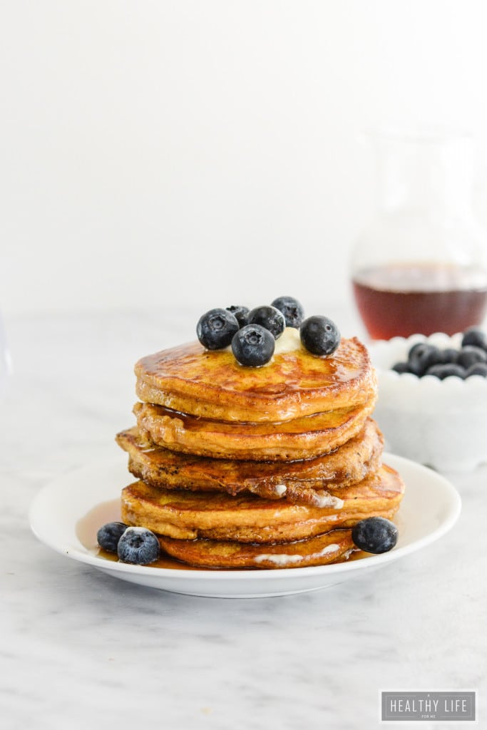 A stack of pumpkin pancakes topped with butter and blueberries with maple syrup.