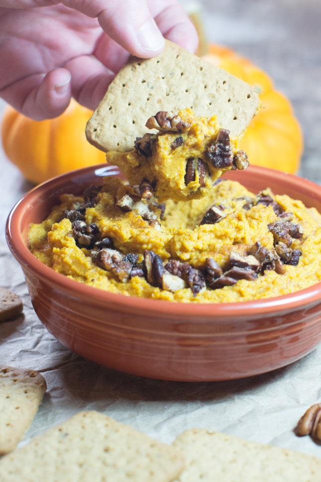 A bowl of pumpkin pie hummus topped with pecans and a graham cracker dipping in. 