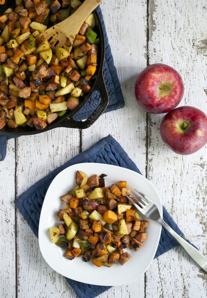 A plate of apple sausage sweet potato hash with a cast iron skillet on the side and fresh apples.