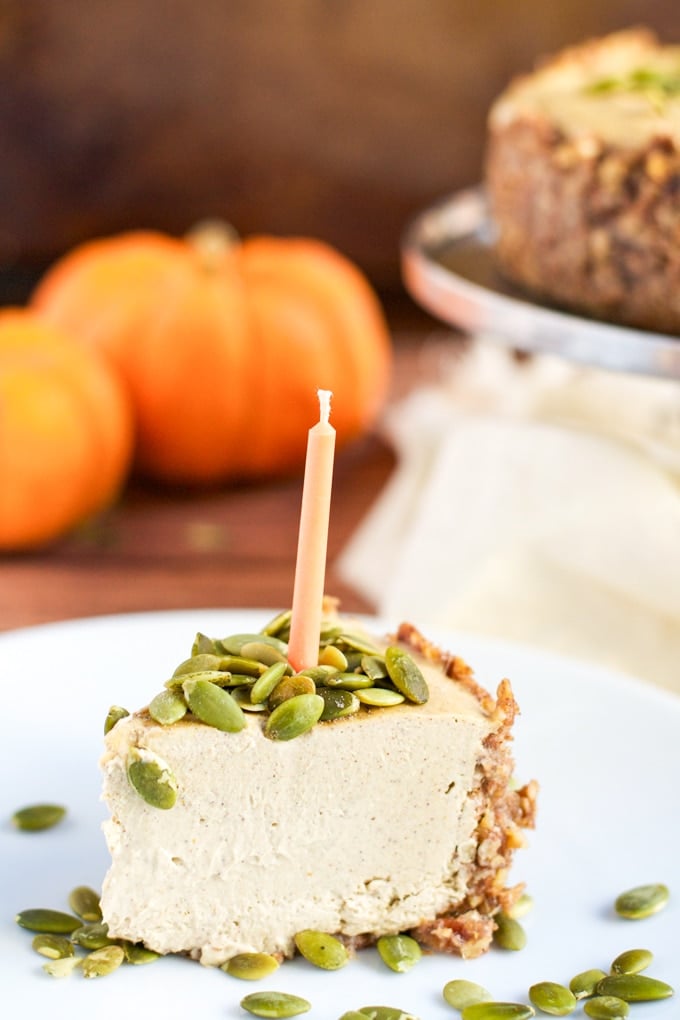 A slice of vegan pumpkin cheesecake topped with pumpkin seeds and an orange candle.