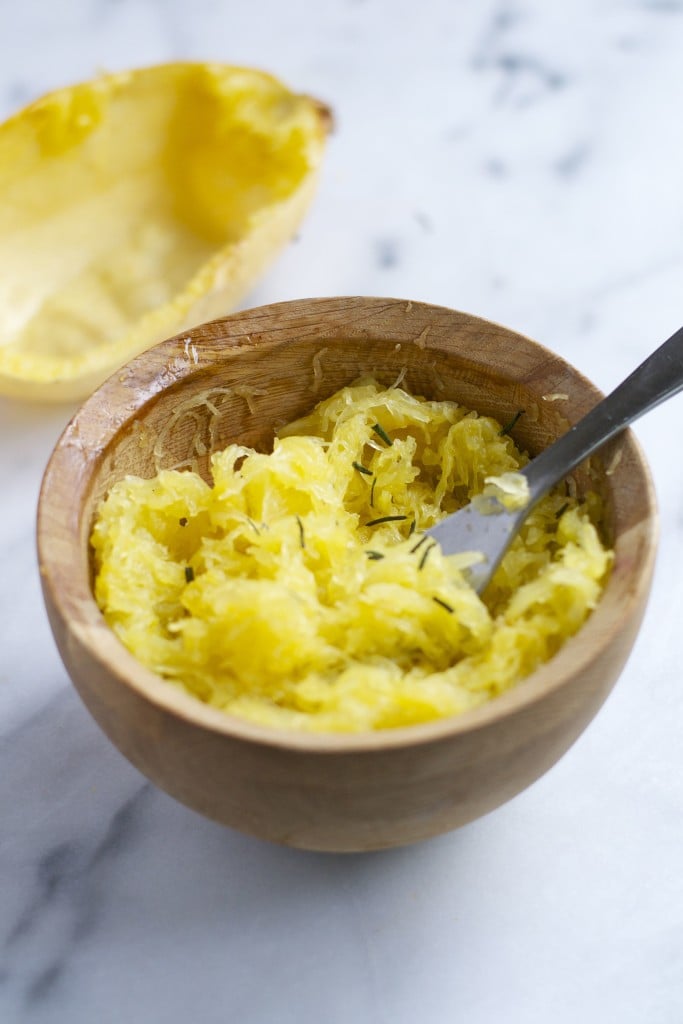 A wodden bowl of roasted spaghetti squash topped with herbs.
