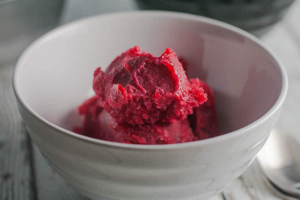 A bowl of cranberry orange sorbet with a spoon next to it.