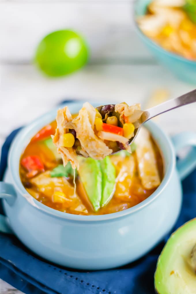 A spoon full of chicken tortilla soup over a bowl of soup.