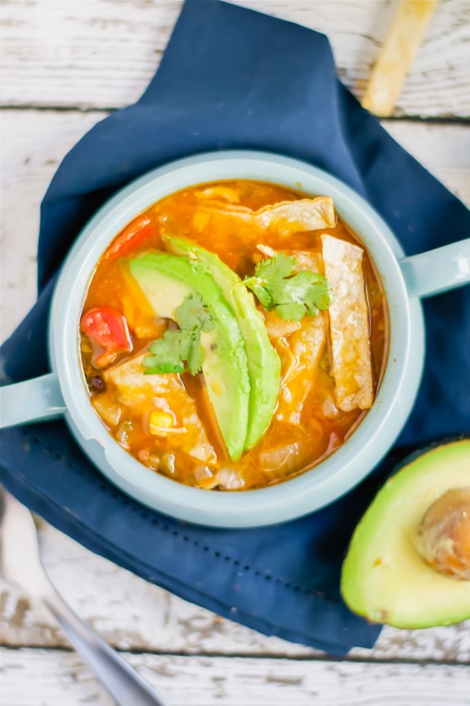 A bowl of chicken tortilla soup topped with avocado slices and cilantro.