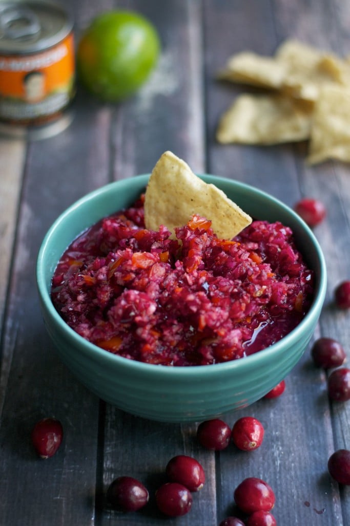 A bowl of cranberry salsa with a tortilla chip in it.