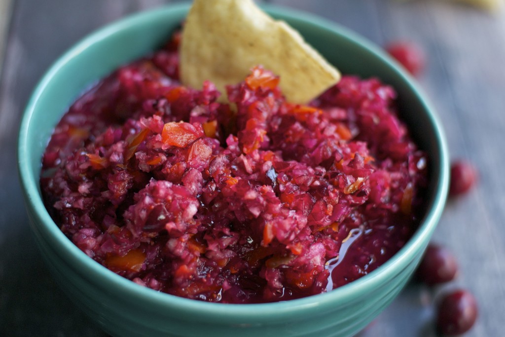 A bowl of cranberry jalapeño salsa with a tortilla chip in it. 