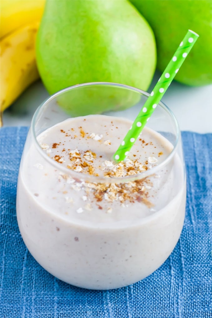 A glass with a ginger peat oatmeal smoothie with a green polka dot straw in it and pears in the background.