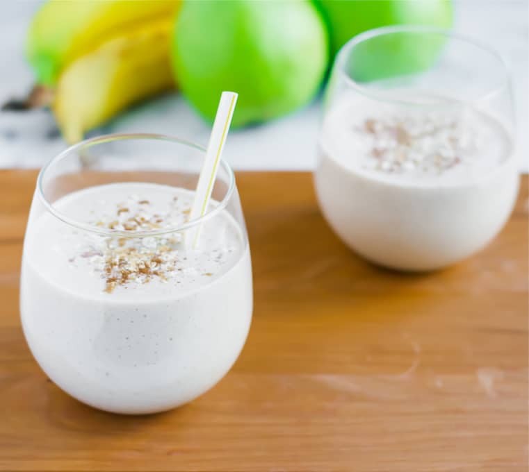 Two glasses of ginger pear oatmeal smoothies on a wood serving board.