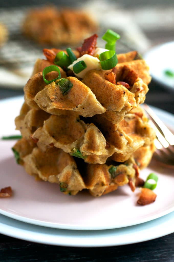 A stack of three mashed potato waffles topped with green onions, bacon and butter. 
