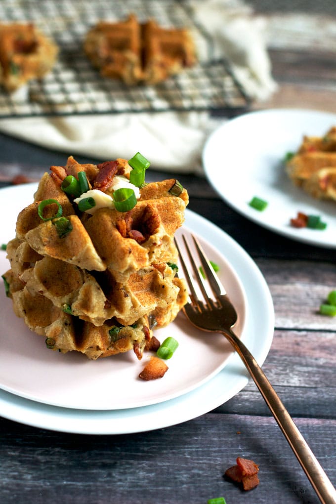 A stack of mashed potato waffles topped with butter, bacon and green onions with a fork on the side.