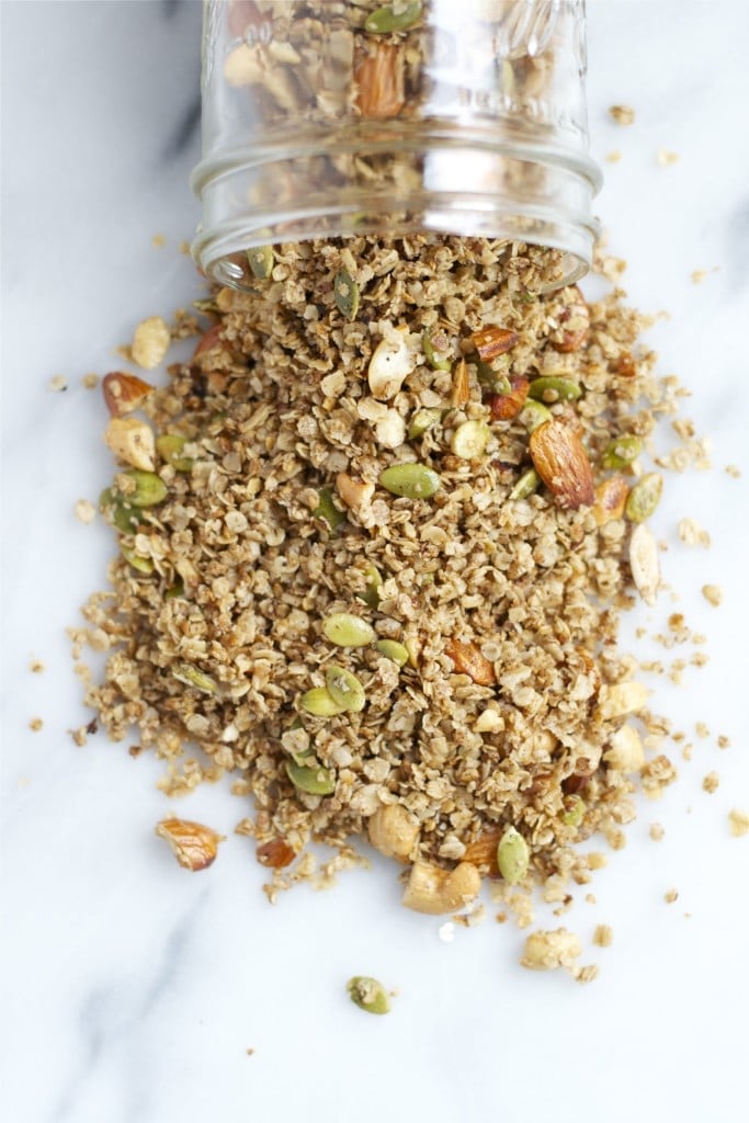 A mason jar of granola with almonds and pumpkin seeds spilling out of it.