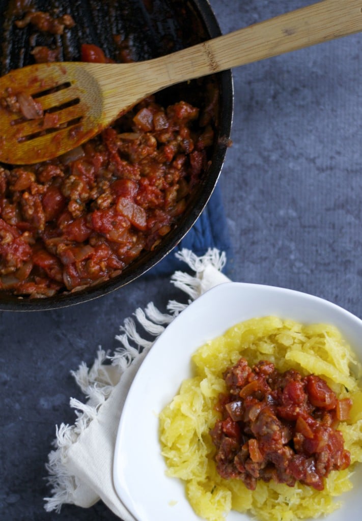 A bowl of spaghetti squash topped with meat sauce and a skillet of meat sauce on the side.