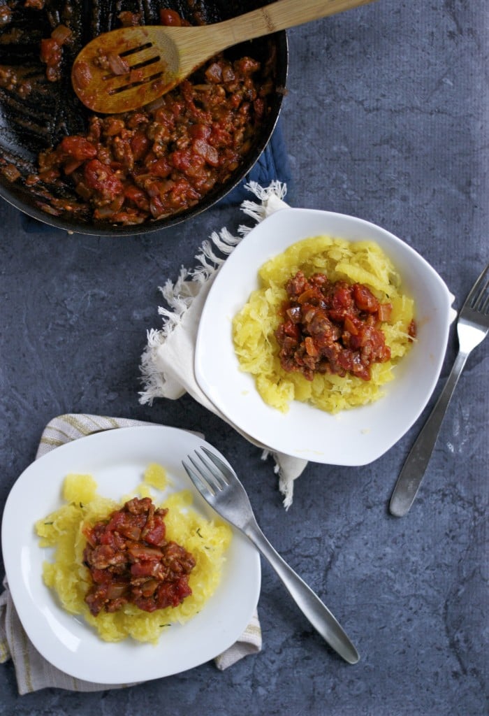 Two bowls of spaghetti squash topped with meat sauce and a skillet of meat sauce to the side.