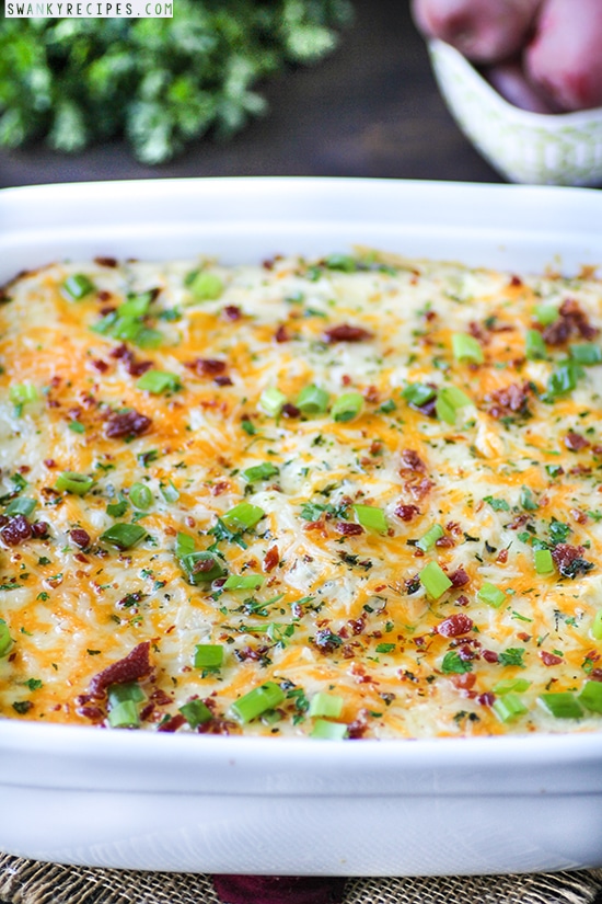 A casserole dish of creamy mashed potatoes topped with bacon, green onions, and cheddar cheese.