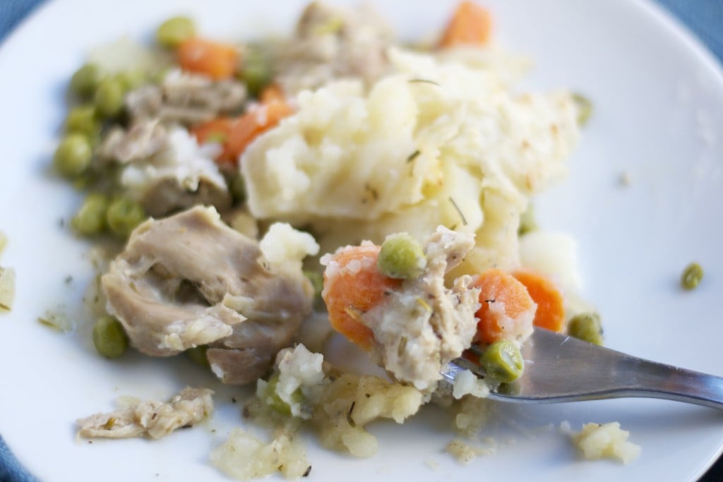 A plate of turkey shepherd's pie with carrots and peas with a fork sticking into it. 