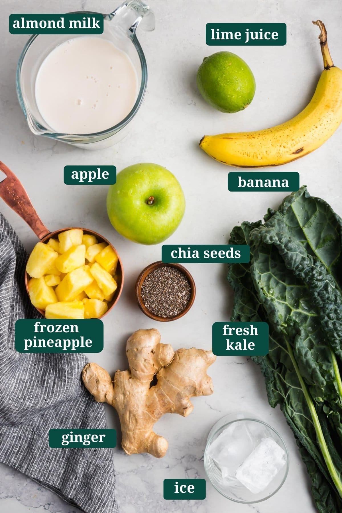 Ingredients for apple kale smoothie: banana, apple, kale, almond milk, chia seed, ginger, ice cubes, lime juice.
