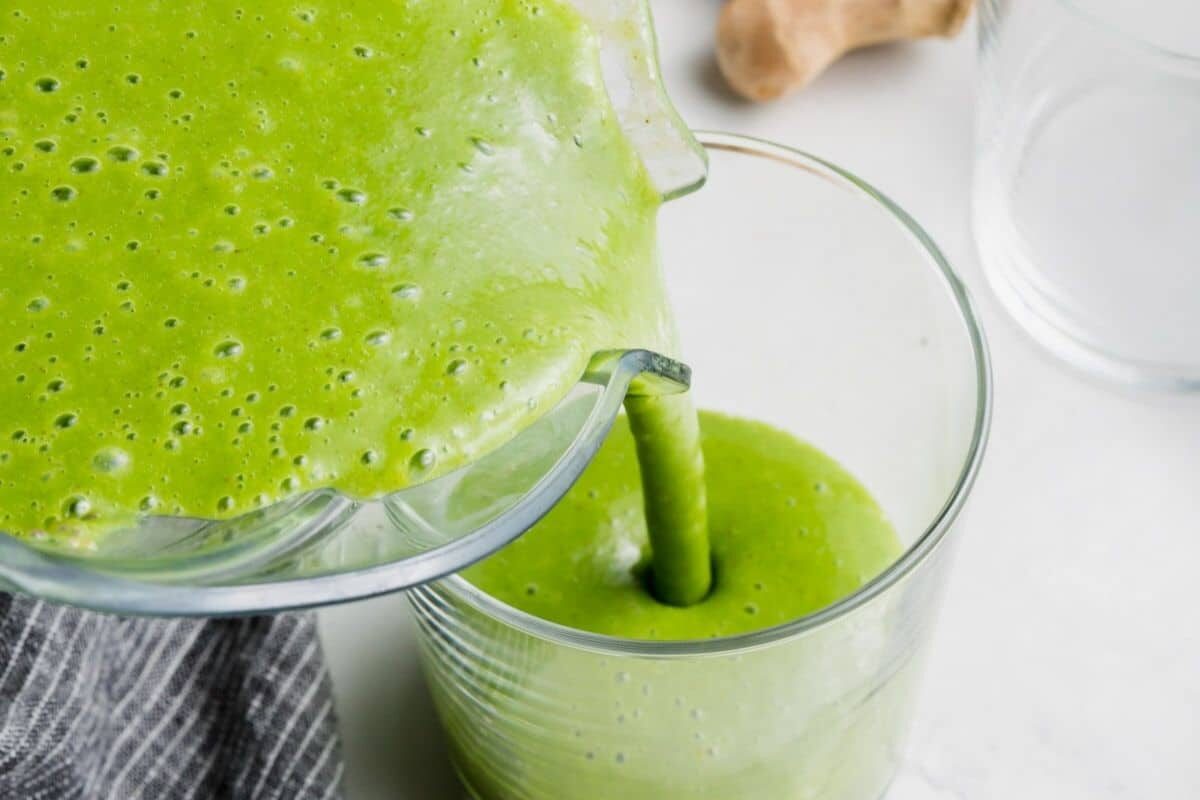 An apple kale green smoothie being poured into a glass.