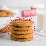 A stack of chewy ginger molasses cookies with a red ribbon and a glass of milk.