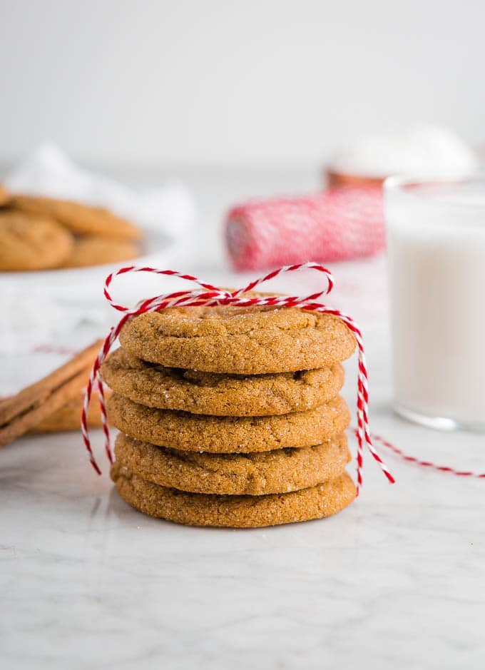 A stack of chewy ginger molasses cookies with a red ribbon and a glass of milk.