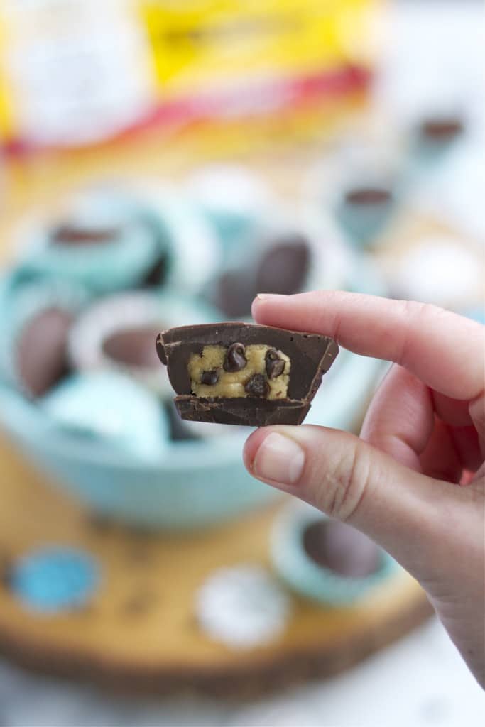 A hand holding a chocolate cover cookie dough cup that has been sliced in half. 