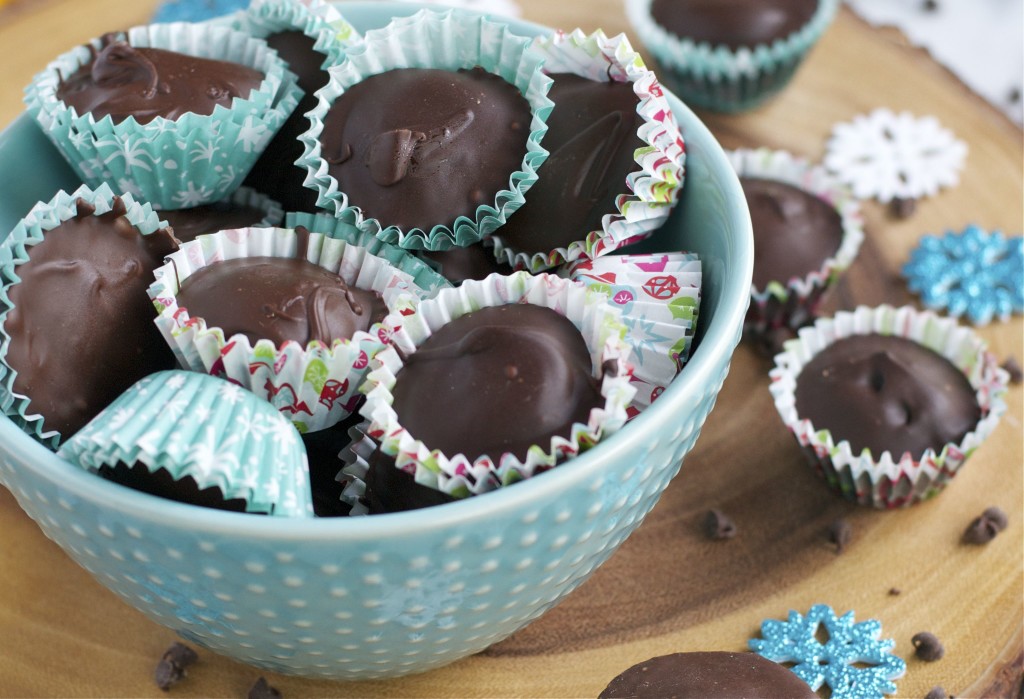 A bowl of chocolate covered cookie dough cups in Christmas themed cupcake liners with paper snowflakes around the surface.
