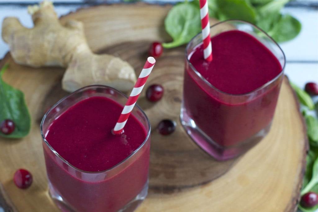 Two glasses of cranberry beet smoothies with red and white striped straws in them.