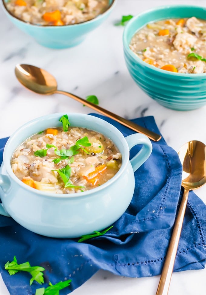 Three bowls of chicken and rice soup topped with fresh parsley and spoons on the side.