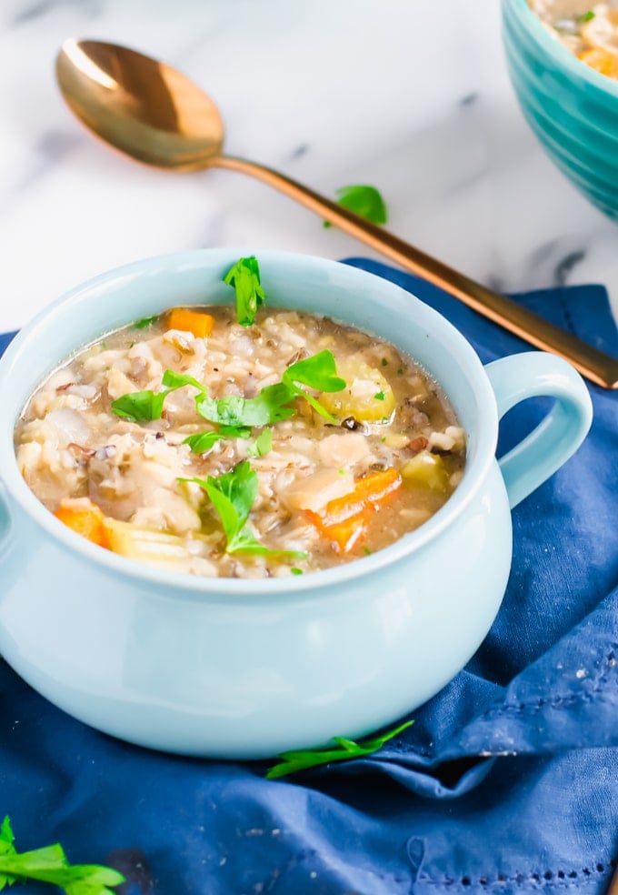 A blue crock of chicken and rice soup topped with fresh parsley on top of a blue napkin.