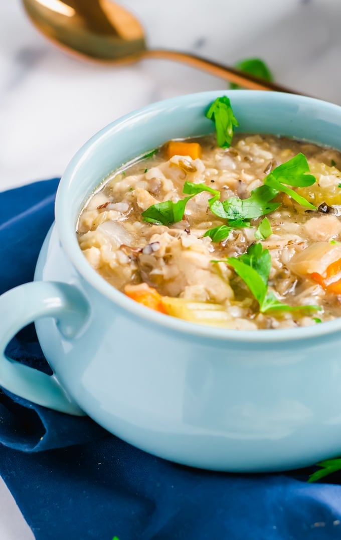 A bowl of chicken and rice soup topped with fresh parsley with a spoon in the background.