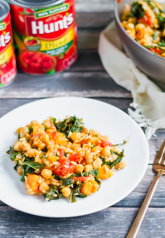 A plate of rice, chickpea, tomato and kale with cans of Hunt's tomatoes in the background.