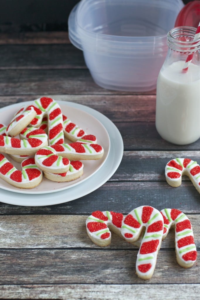 Candy cane shaped cookies on a platter with a glass of milk and more candy cane cookies on the side.