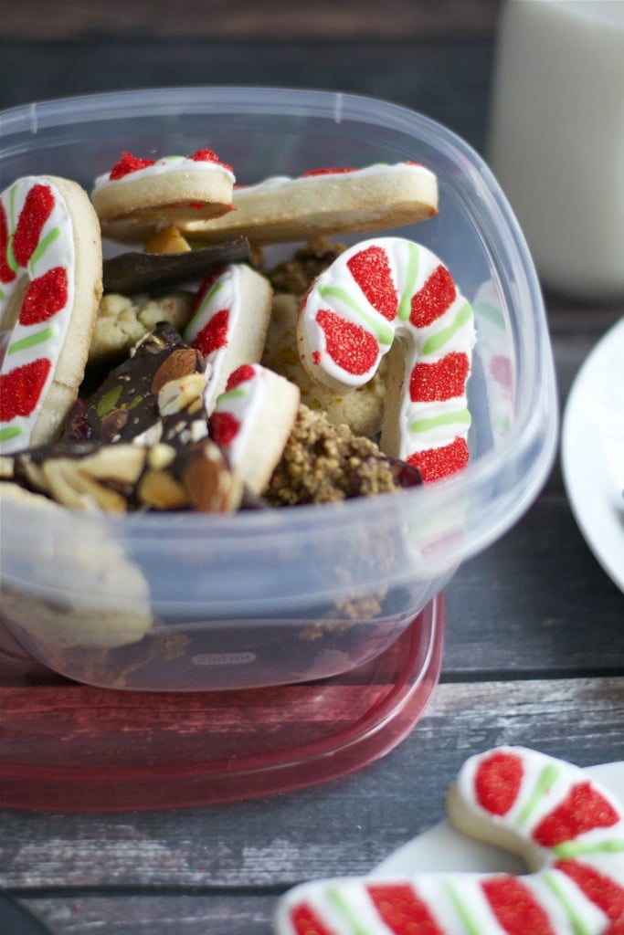 A tupperware filled with an assortment of cookies including candy cane cookies and chocolate bark.