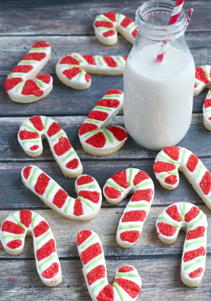 Candy cane shaped sugar cookies facing different directions with a glass of milk with a striped straw.