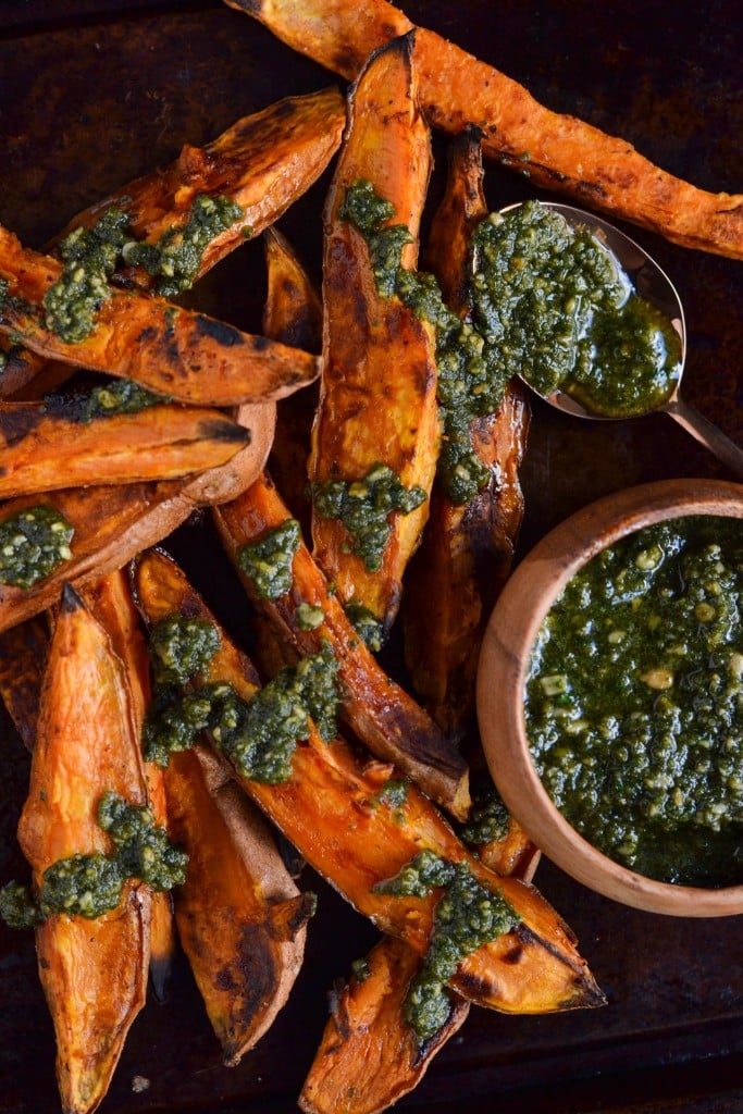 Sweet Potato Wedges topped with a drizzle of Vegan Parsley Pesto on a baking sheet.
