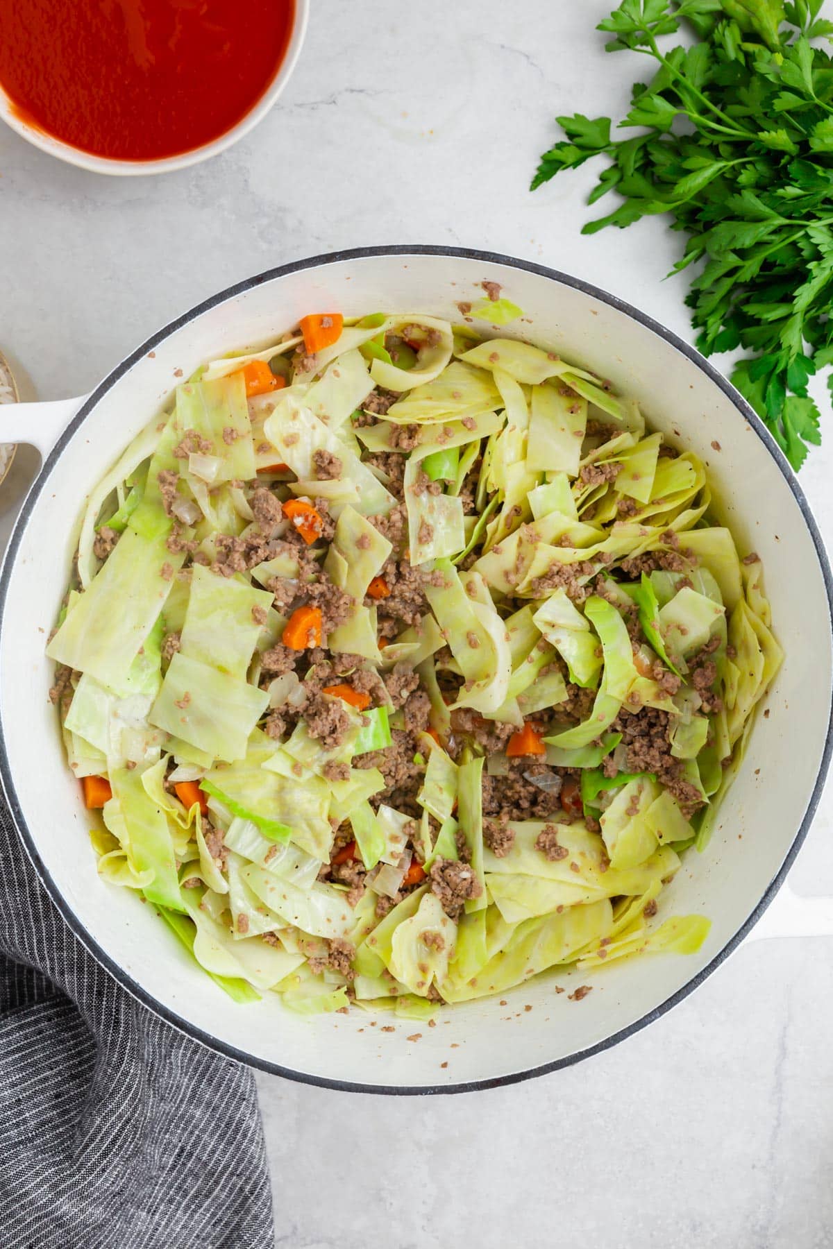 A dutch oven of cooked ground beef, diced carrots and shredded cabbage that have been mixed together.
