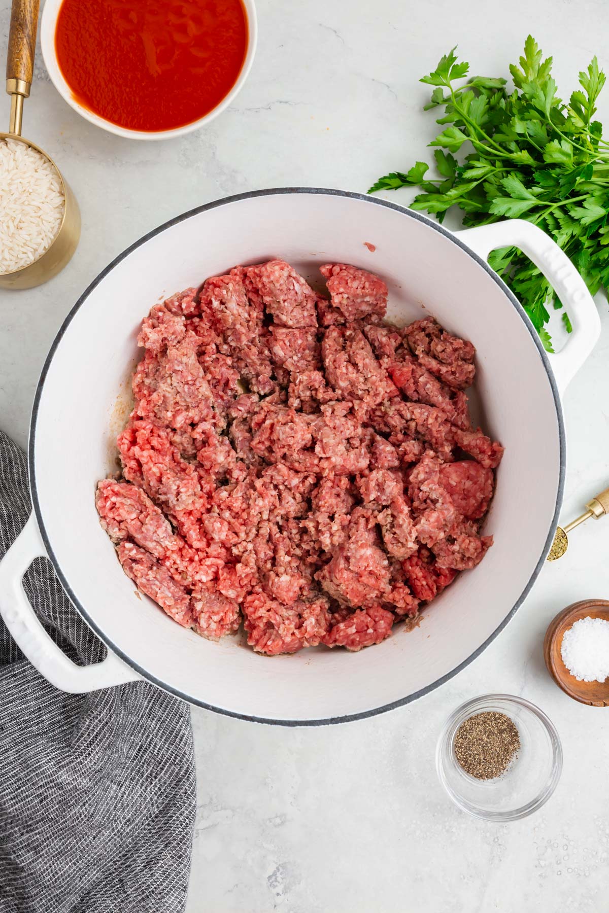 A white dutch oven with raw ground beef in it that is starting to cook.